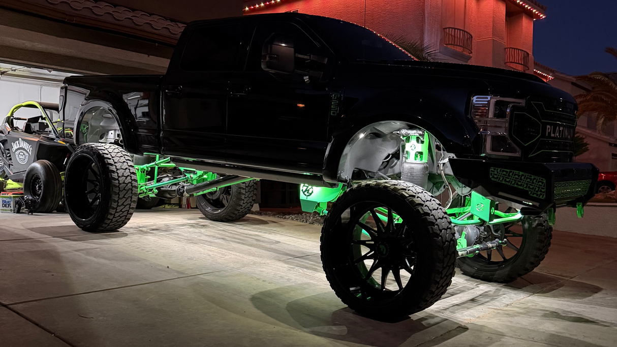 Large black off-road vehicle with green wheels in a driveway at night.